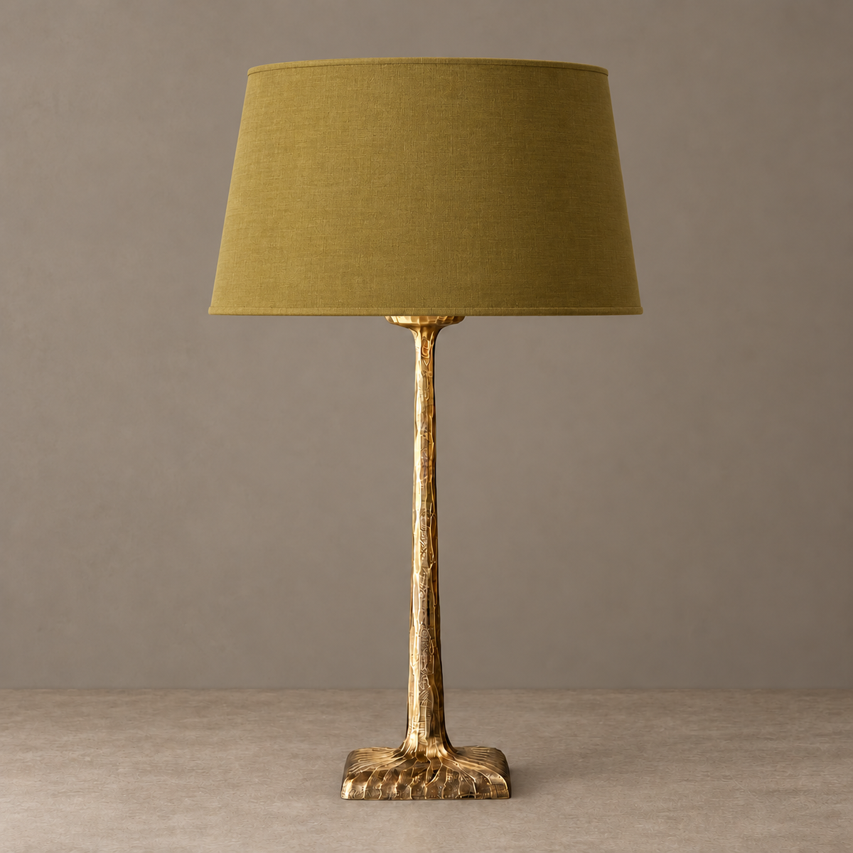 Hammered brass table lamp with an olive tapered fabric shade, unlit.
