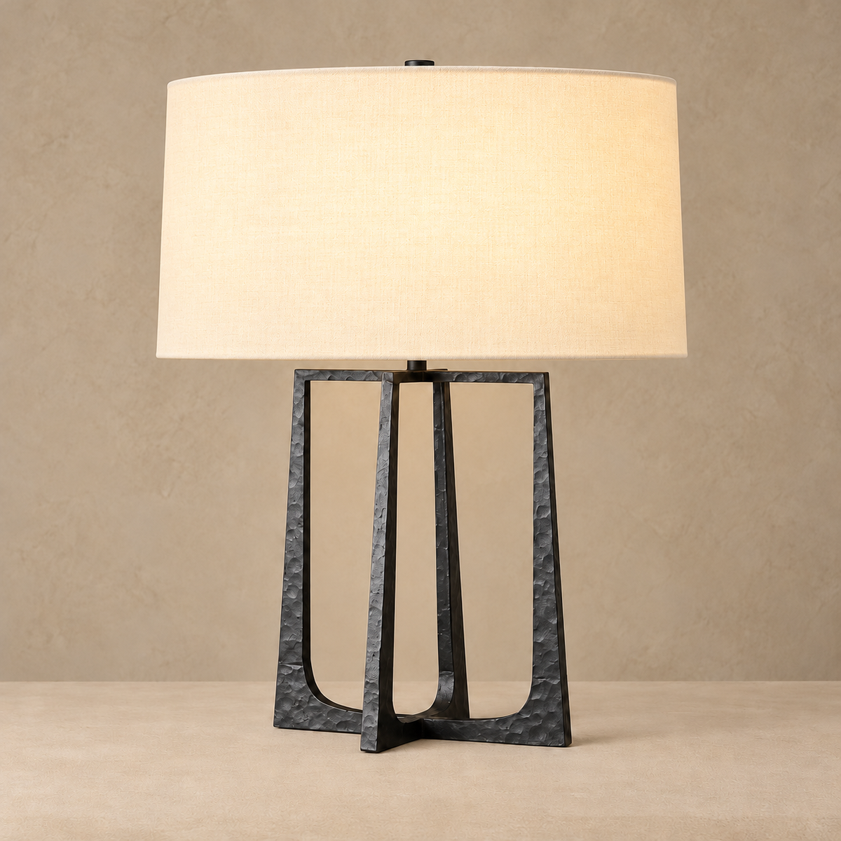 Hammered black stainless steel split-frame table lamp, illuminated, on a beige background.