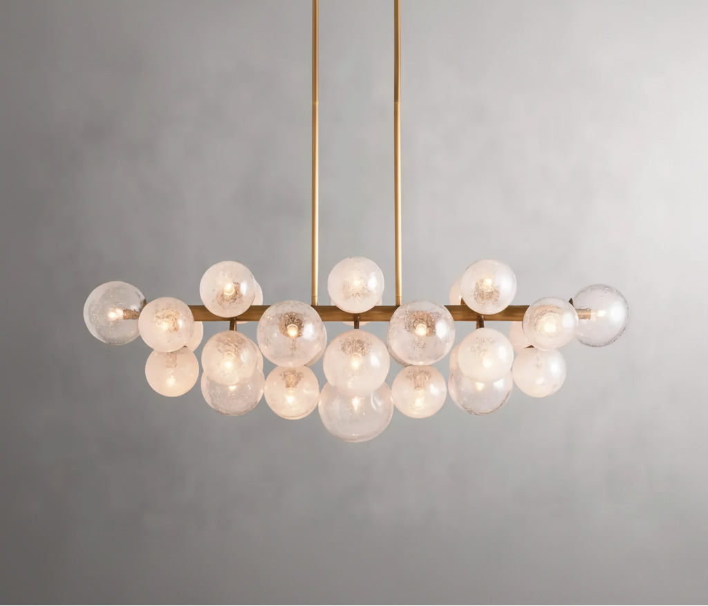 A modern linear chandelier with a brushed gold metal frame and multiple clear glass globes, shown lit against a neutral gray background.