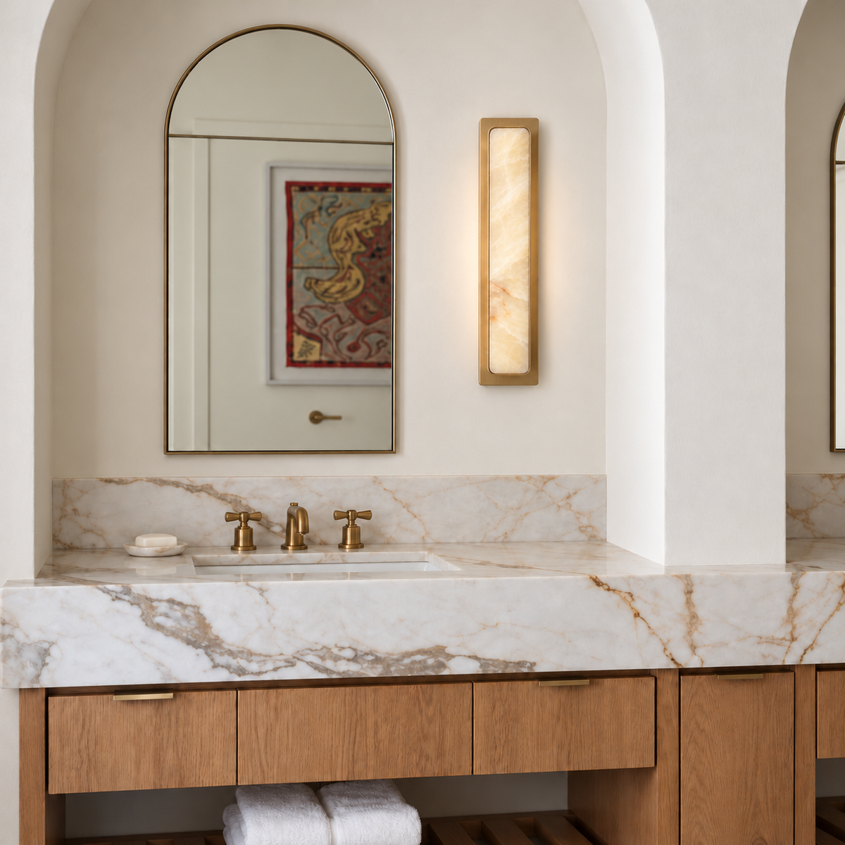 Mont honey onyx and brass wall sconce beside an arched bathroom mirror.