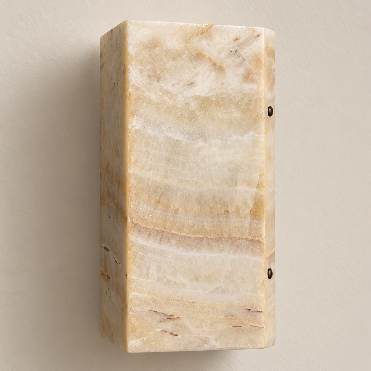 Close-up of the onyx wall sconce’s layered honey and cream stone surface and curved corner.