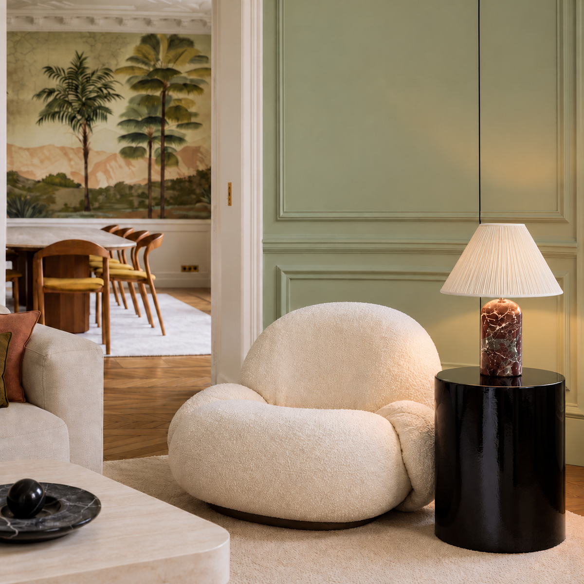 Red marble table lamp with a pleated shade on a black side table beside a cream armchair.