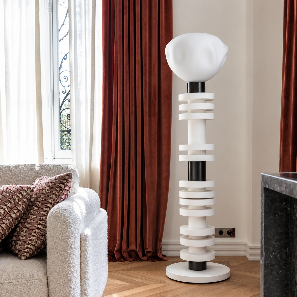 White stacking floor lamp beside red curtains, a boucle chair and a marble fireplace.