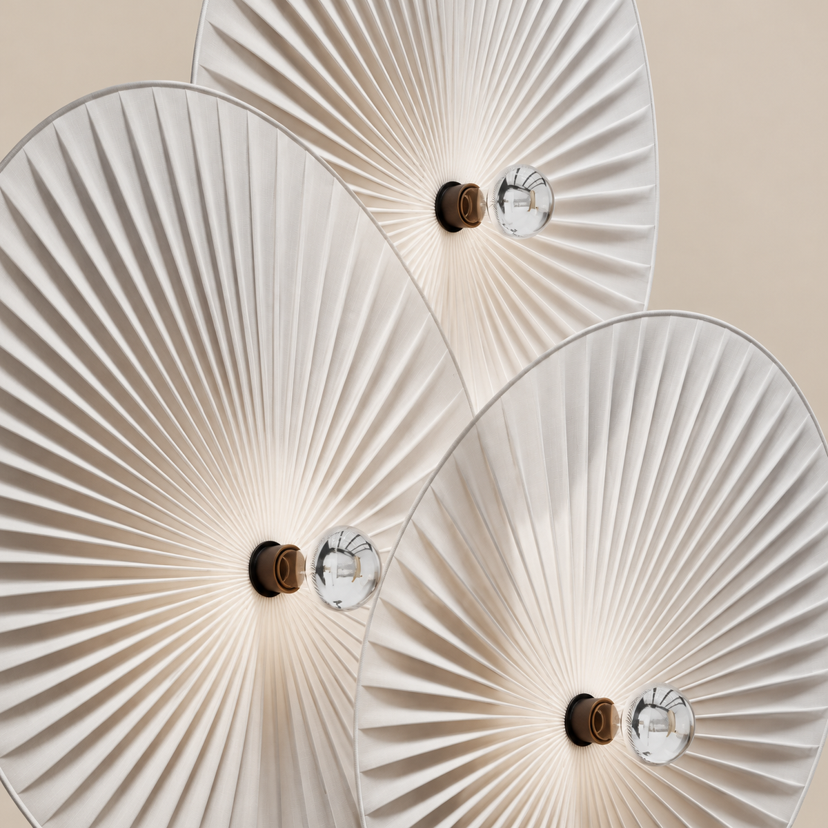 Close view of Svelo's white pleated linen shades, bound edges and silver-capped bulbs.